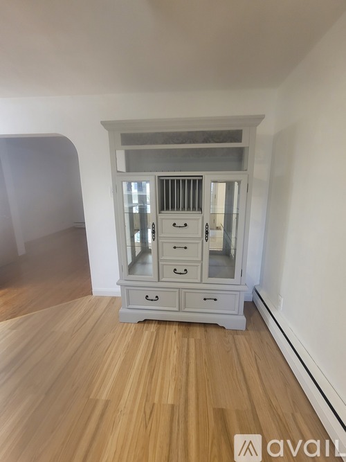 A wooden cabinet with glass doors and drawers is in a room with wooden flooring.
