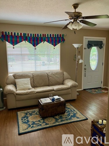 A living room with a beige couch, a ceiling fan, and a rug.