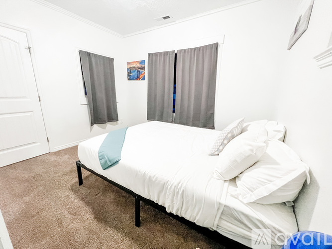 A bed with a white sheet and a blue pillow is in the center of a room with white walls.