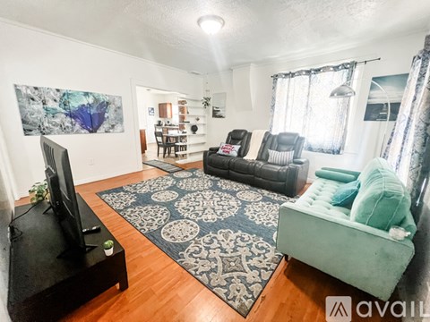 A living room with a rug, a couch, a chair, a television and a painting on the wall.