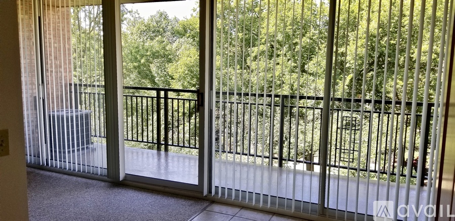 A balcony with a metal railing and glass doors leading to a wooded area.