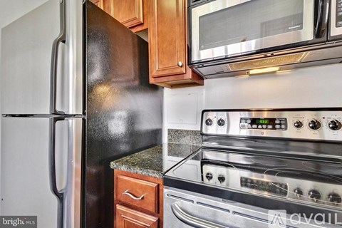 A kitchen with a black refrigerator, a stove with a digital display, and wooden cabinets.