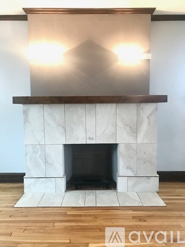 A white marble fireplace with a wooden mantle and a wooden floor.