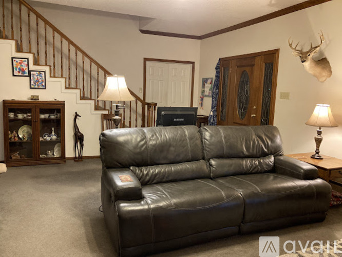 A black leather couch in a living room with a staircase in the background.