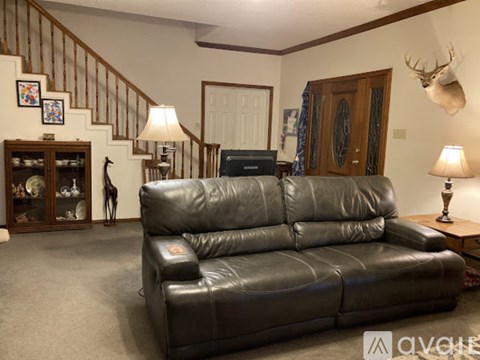 A black leather couch in a living room with a staircase in the background.