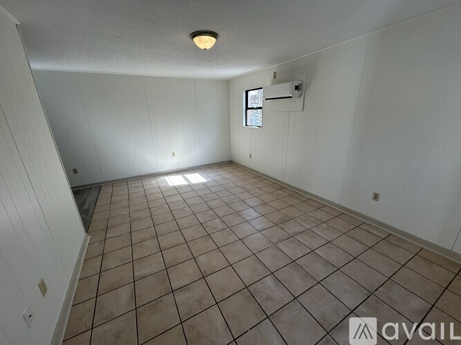 A room with tiled flooring and a window with an air conditioning unit on the wall.