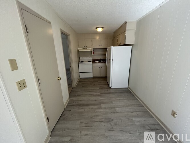 A kitchen area with a white fridge and wooden flooring.