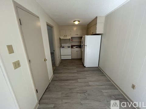 A kitchen area with a white fridge and wooden flooring.