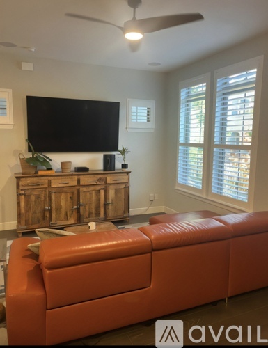 A living room with a television, a wooden cabinet, and a brown leather couch.