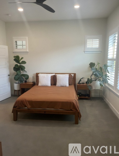 A bedroom with a bed, nightstand, and a plant.