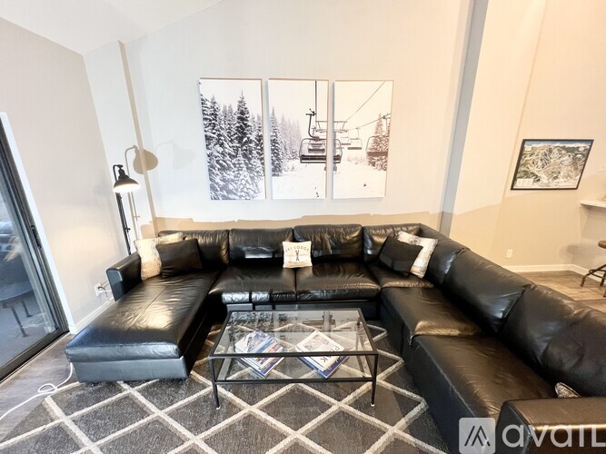 A black leather sectional sofa with a glass coffee table in front of a window with a view of a ski lift.