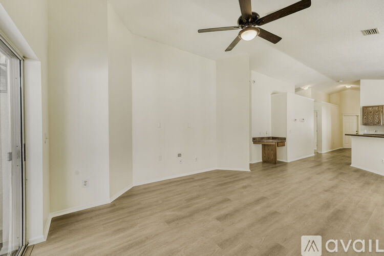 A spacious room with a ceiling fan and light fixture, and a wooden table in the corner.