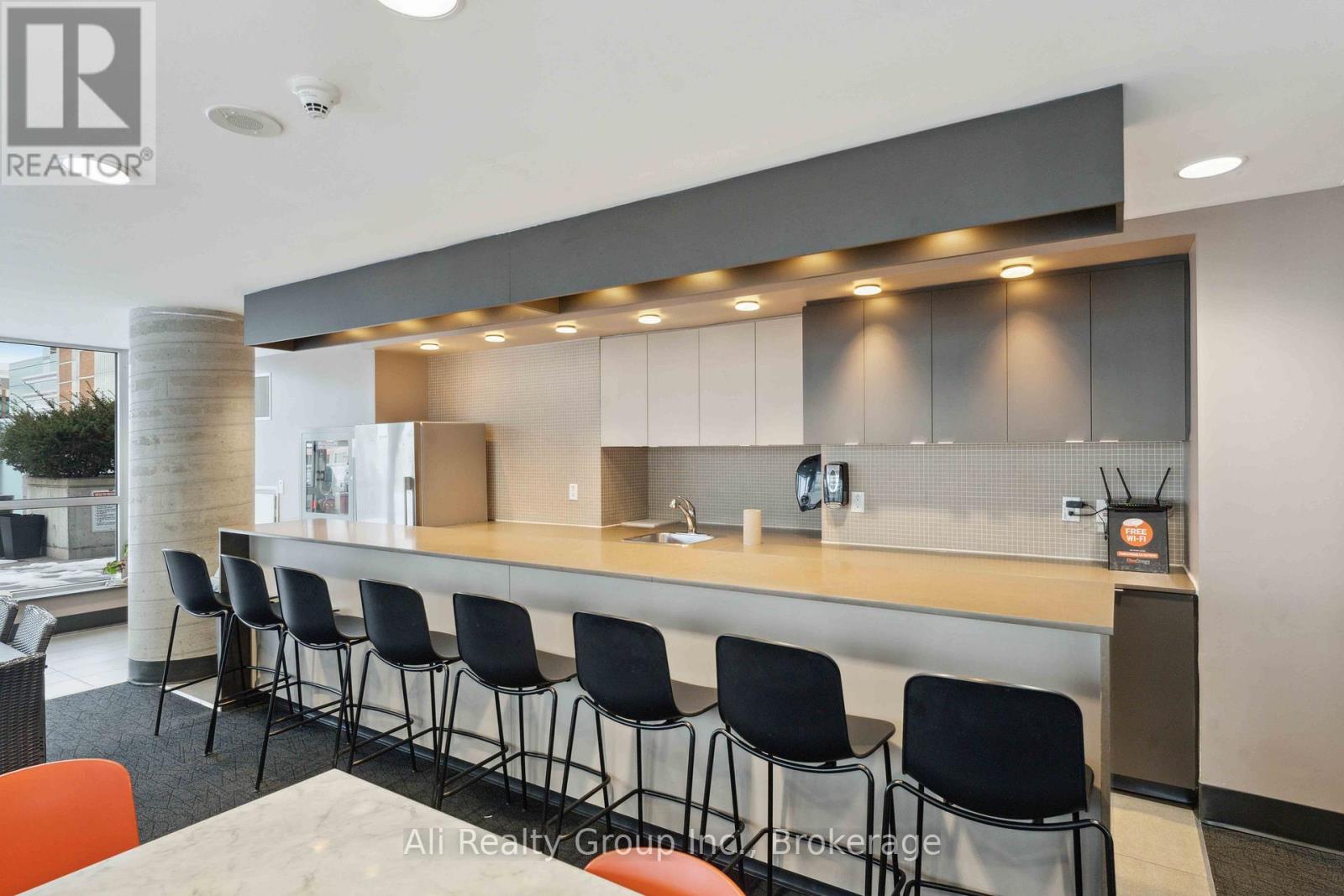 A modern kitchen with a long counter and black chairs.