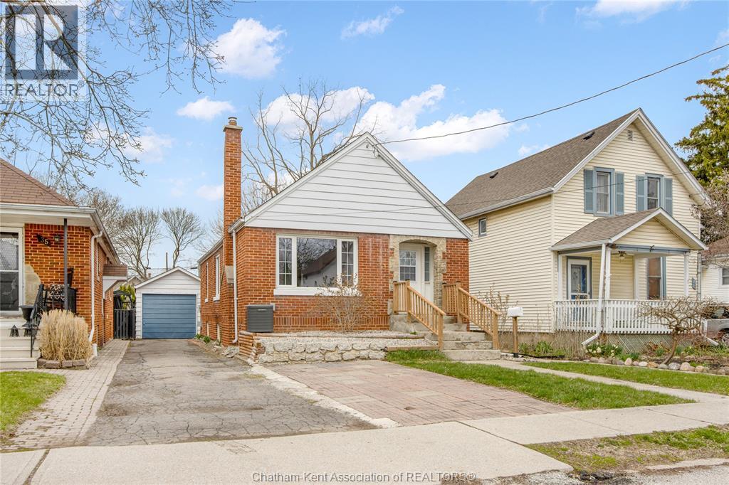 A house with a brick chimney is in front of a house with a white fence.