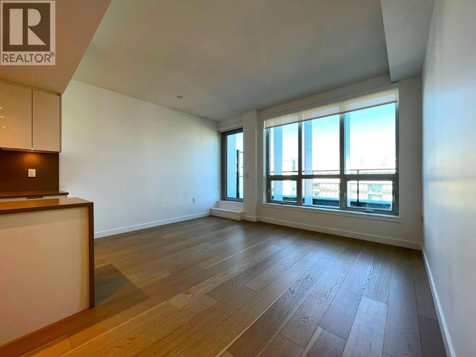 A spacious room with wooden flooring and large windows.