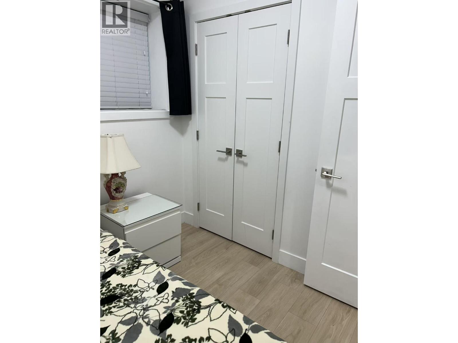 A white bedroom with a bed, nightstand, and wardrobe.