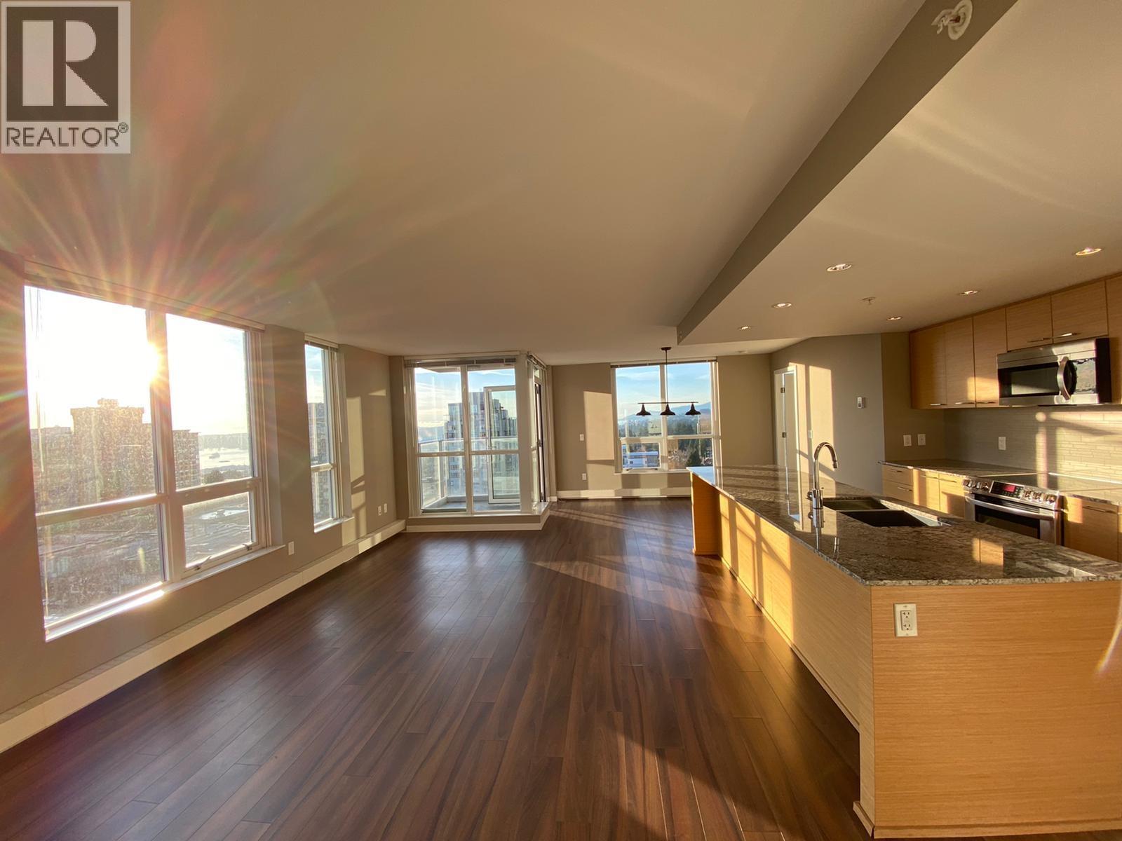 A spacious living room with wooden floors and a large window overlooking the city.