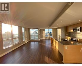 A spacious living room with wooden floors and a large window overlooking the city.