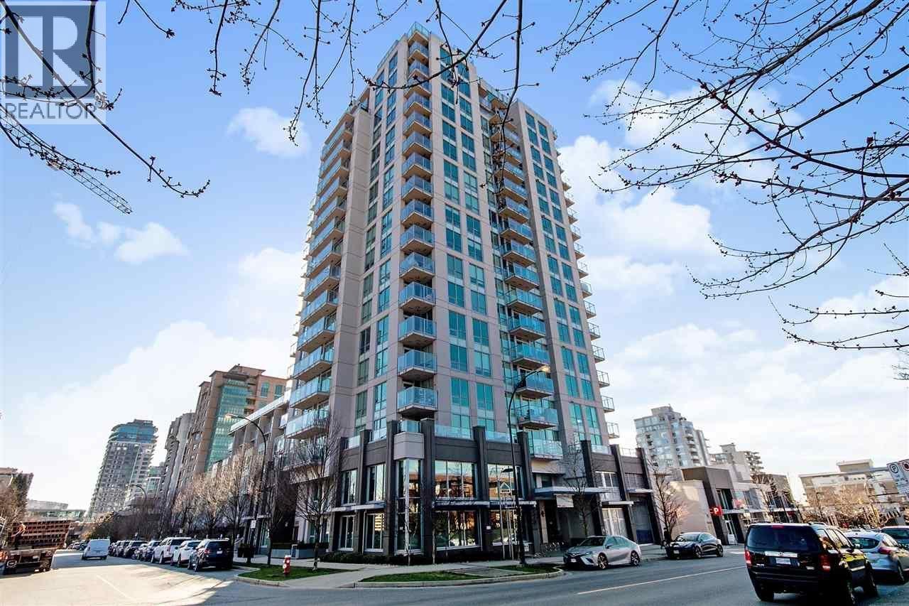 A tall building with many windows is surrounded by trees and cars.