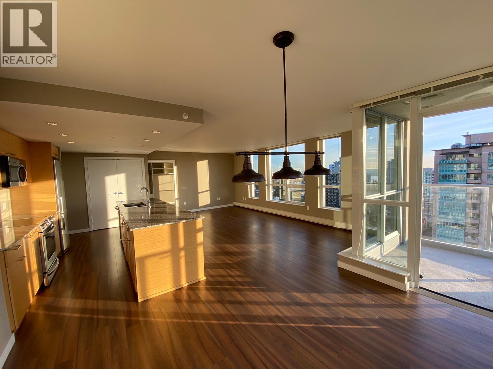 A spacious kitchen and living room with wooden floors and a large window.