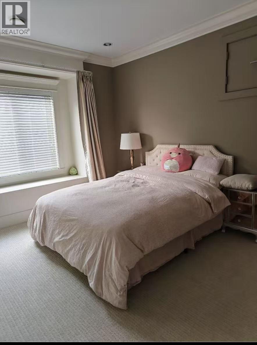 A bed with a white comforter and pink pillows sits in a room with a window.