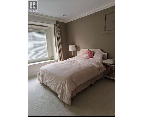 A bed with a white comforter and pink pillows sits in a room with a window.