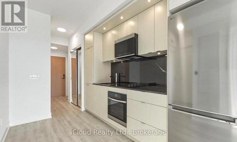 A modern kitchen with a stainless steel refrigerator and black countertops.