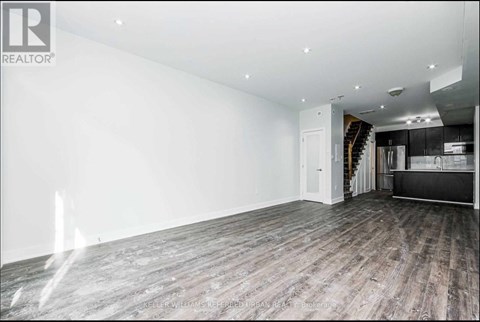 A spacious room with wooden flooring and a staircase in the background.