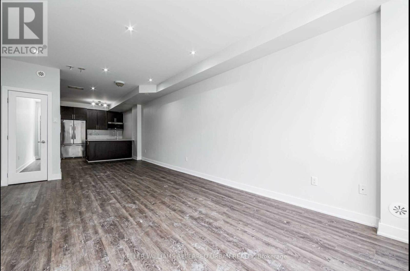 A spacious room with wooden flooring and a white wall.