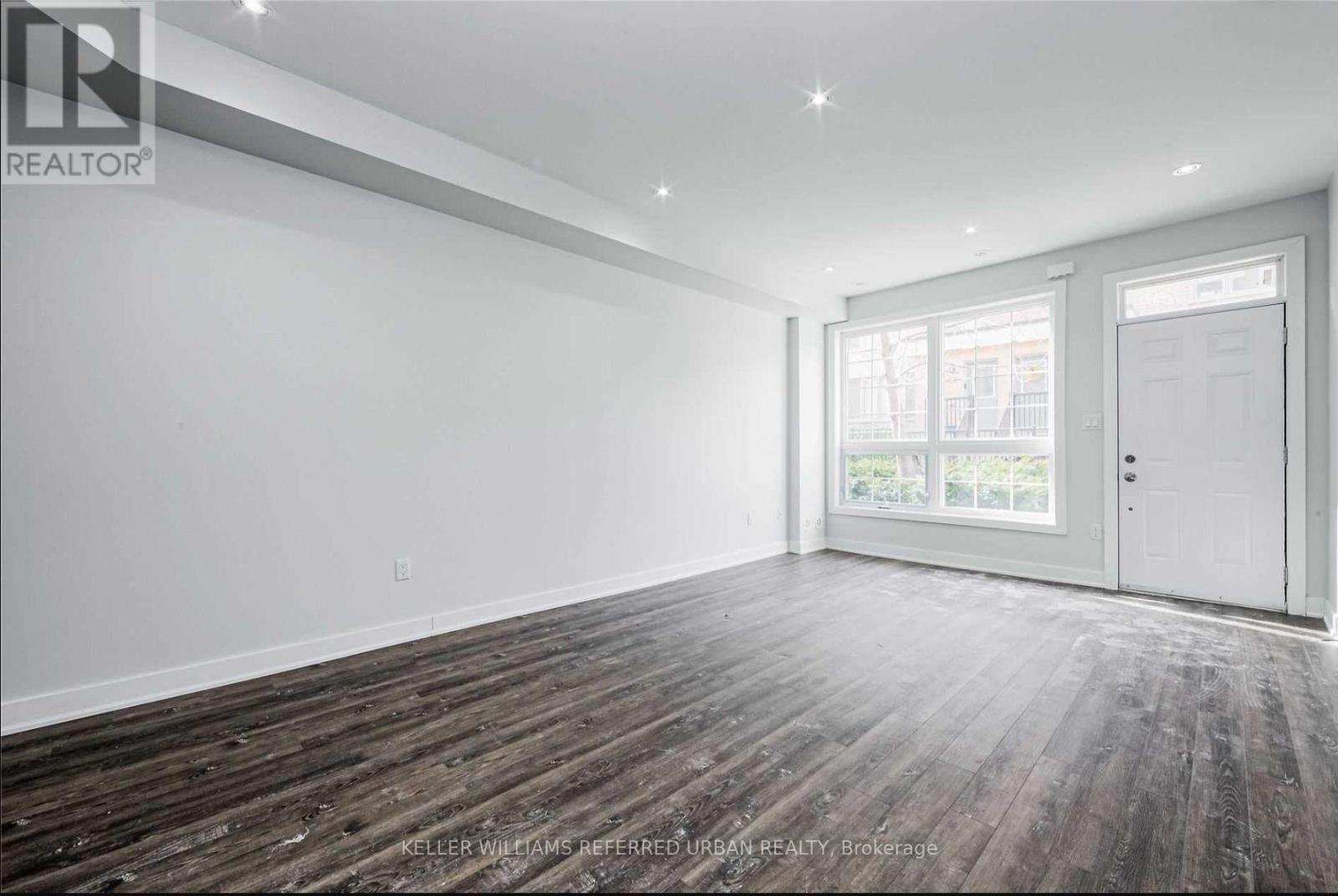 A spacious room with wooden flooring and a large window.