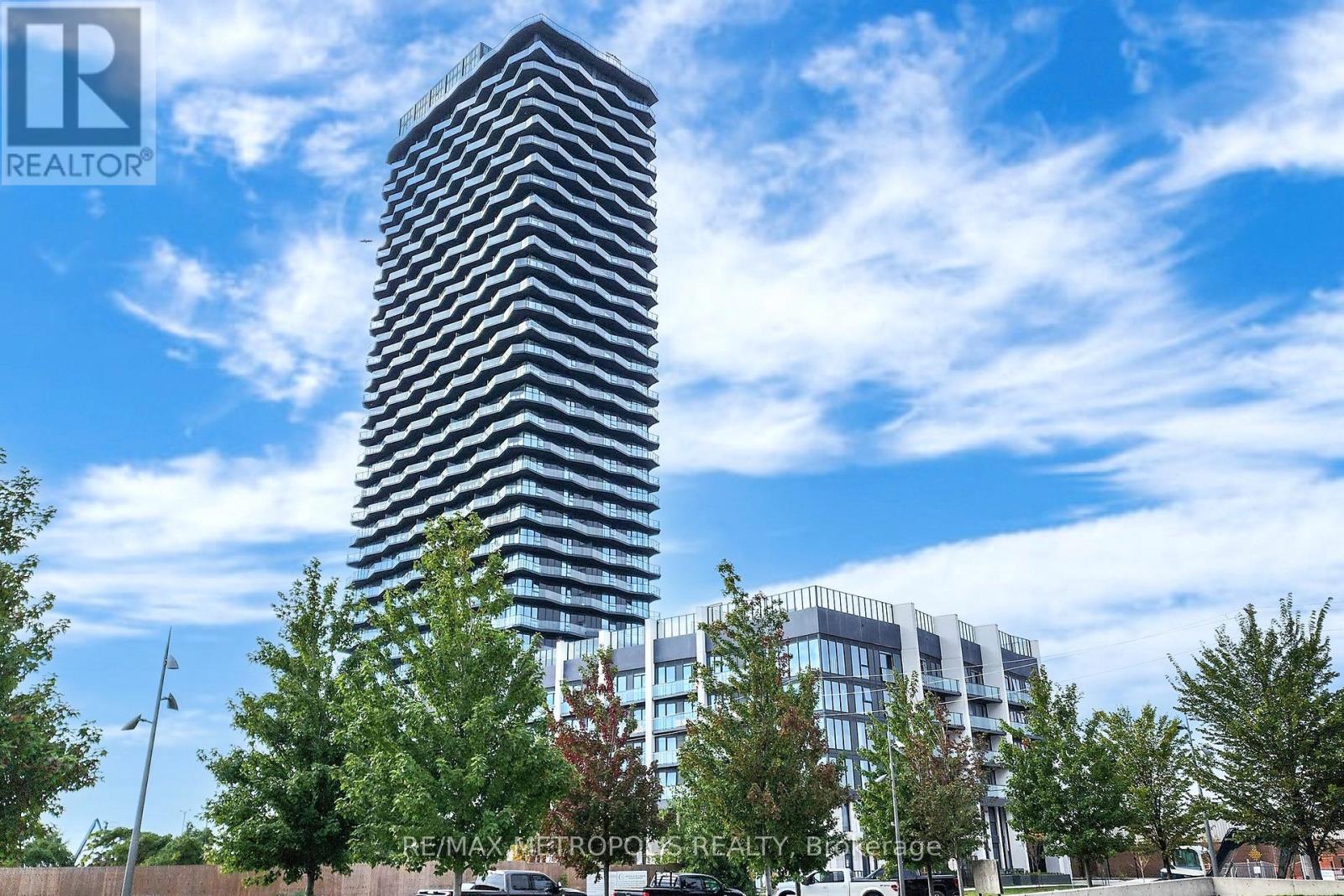 A tall building with a glass facade stands in front of a row of trees.