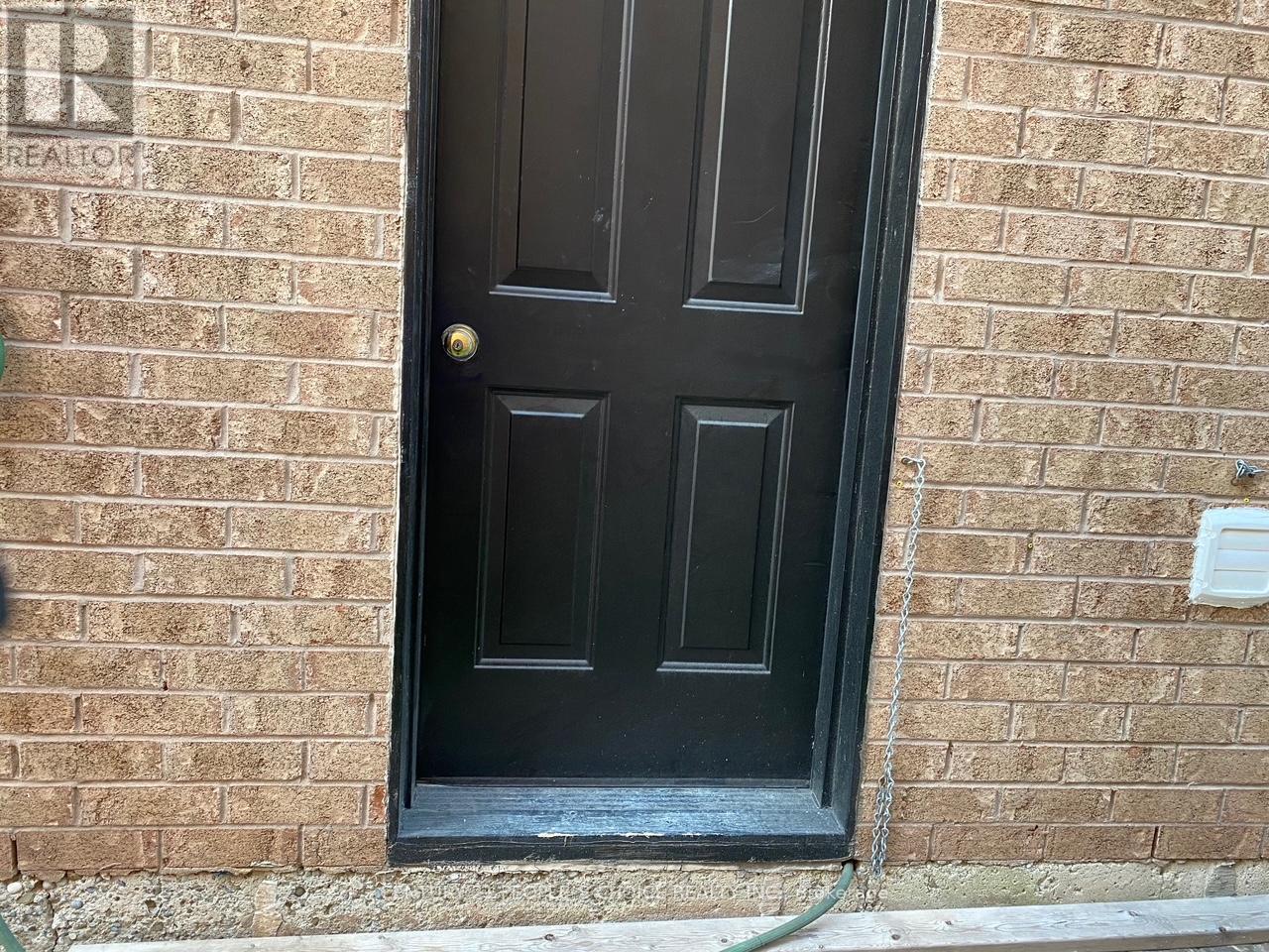 A black door with a gold handle is set in a brick wall.