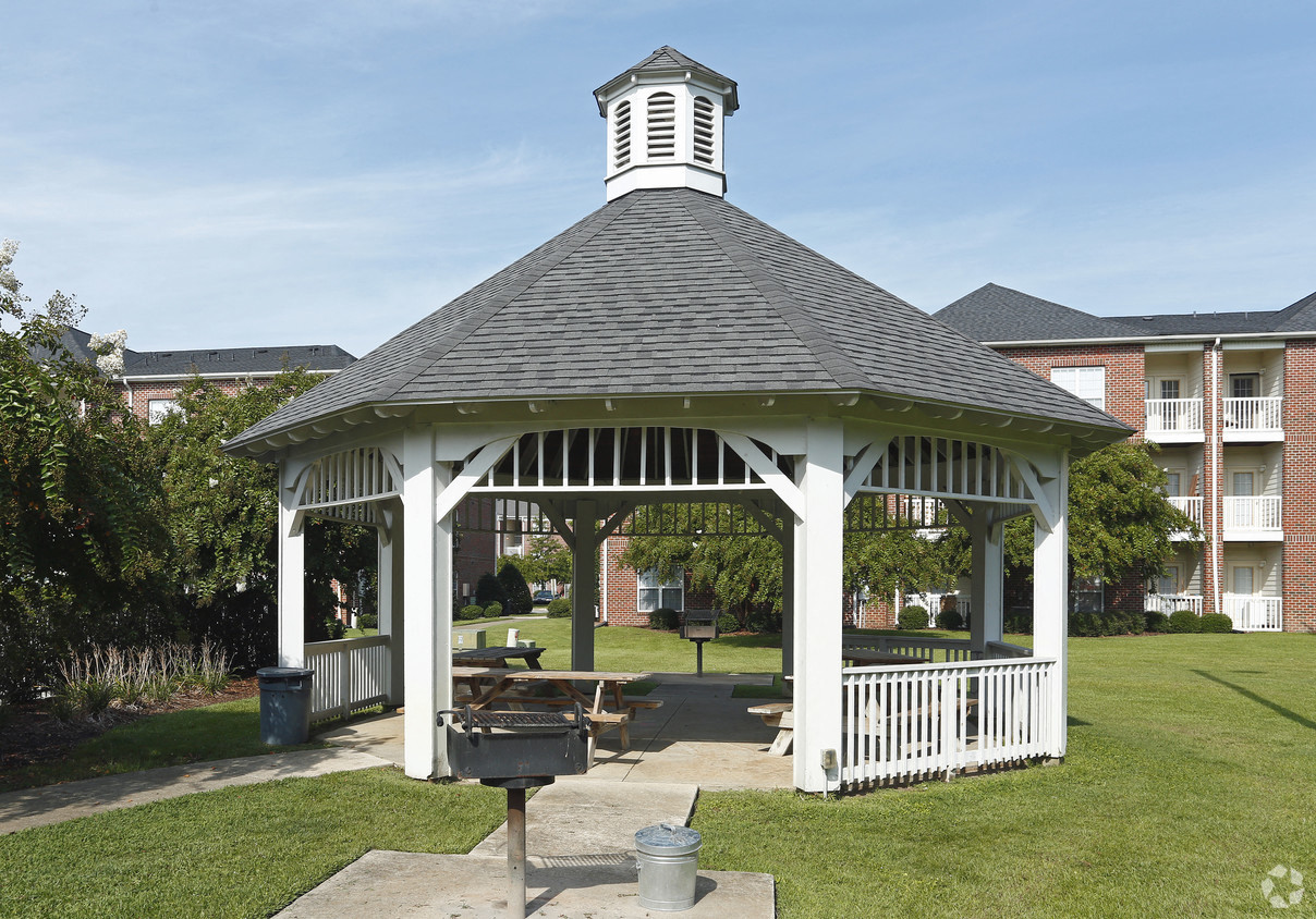 A gazebo with a white frame and a black roof is surrounded by a white picket fence.
