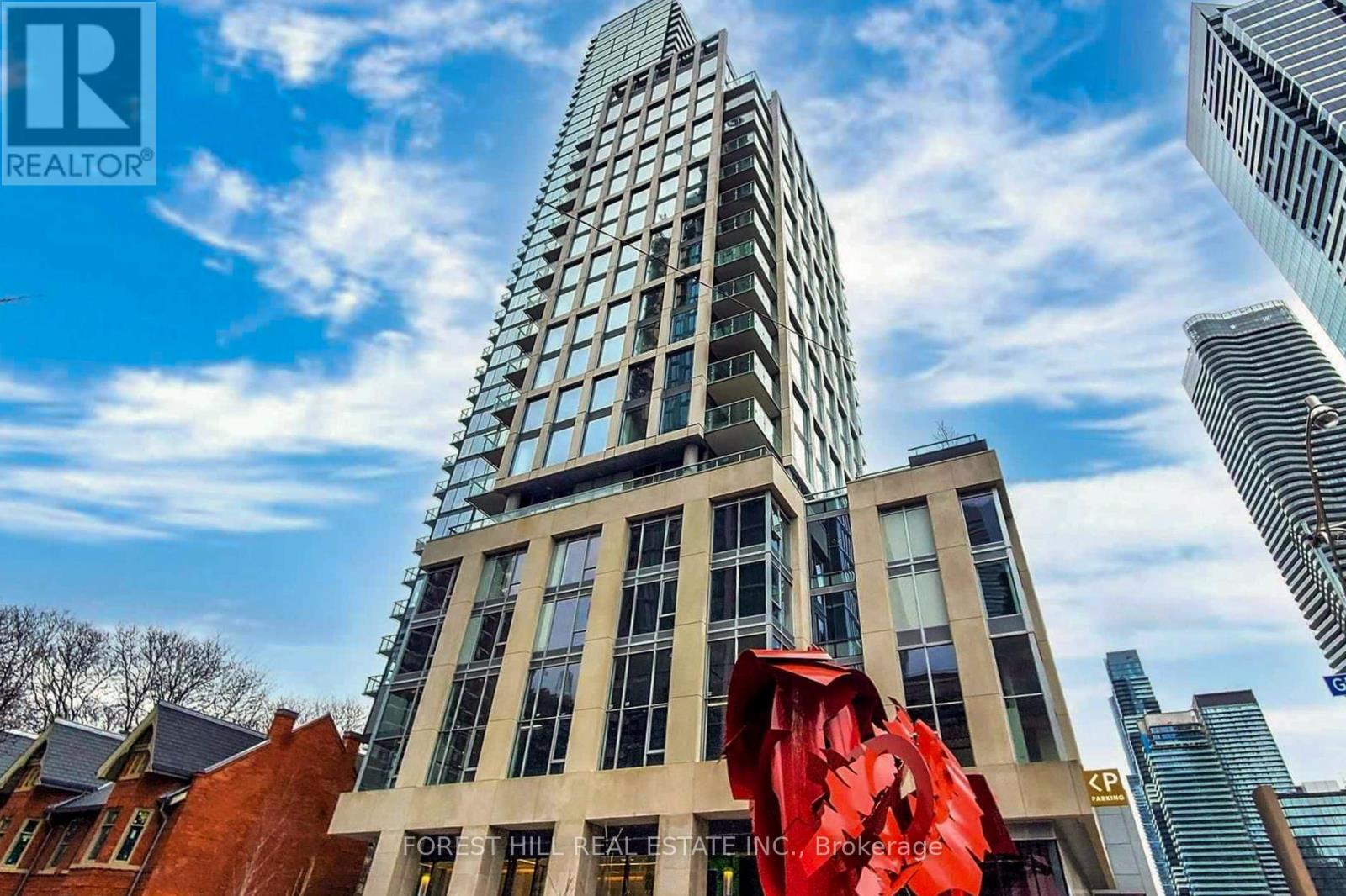 A tall building with a glass facade stands in front of a red sculpture.