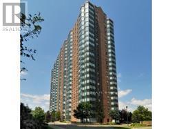 A tall building with many windows is surrounded by trees.