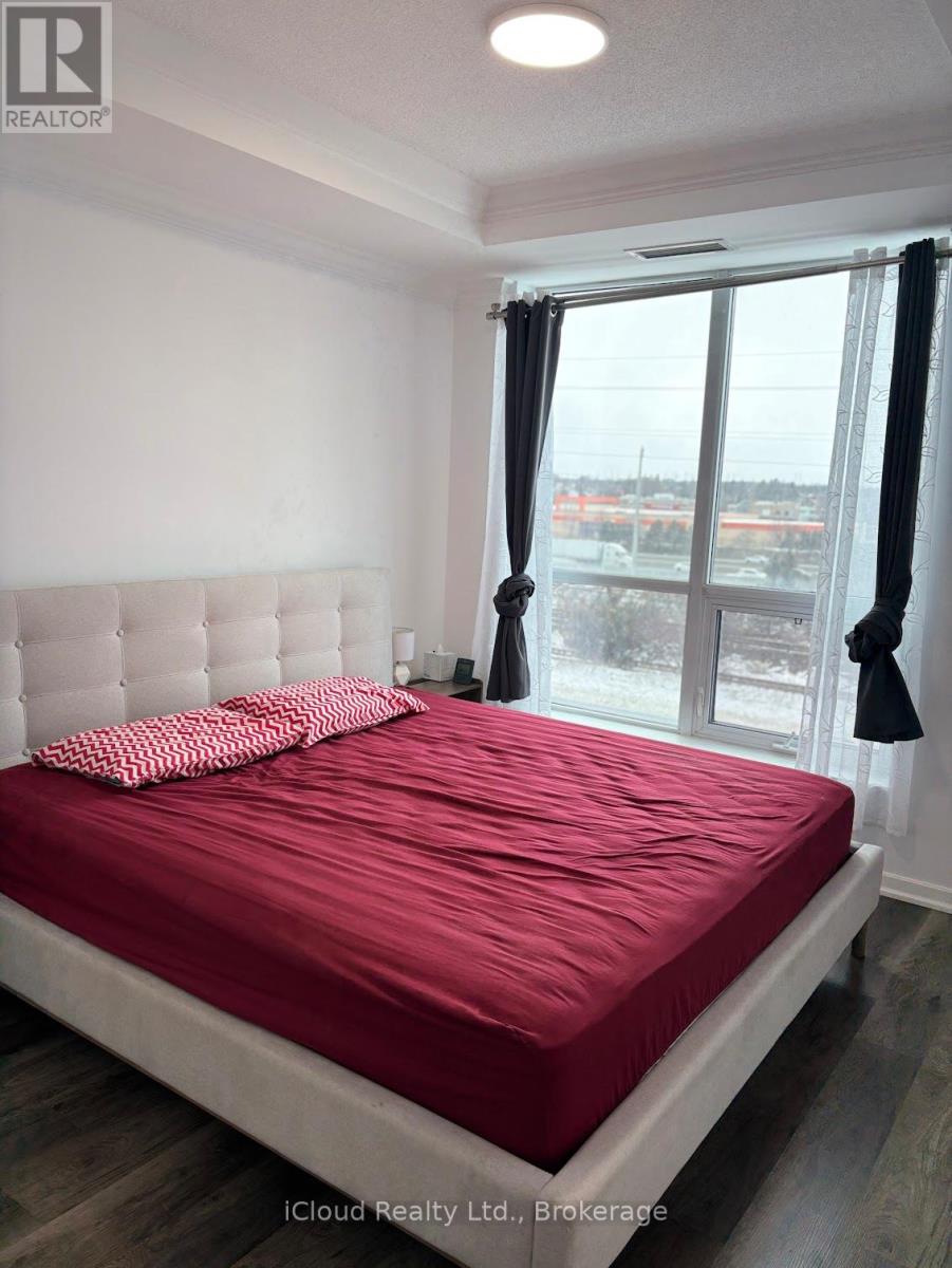 A bedroom with a red bedspread and a window with a view of a parking lot.