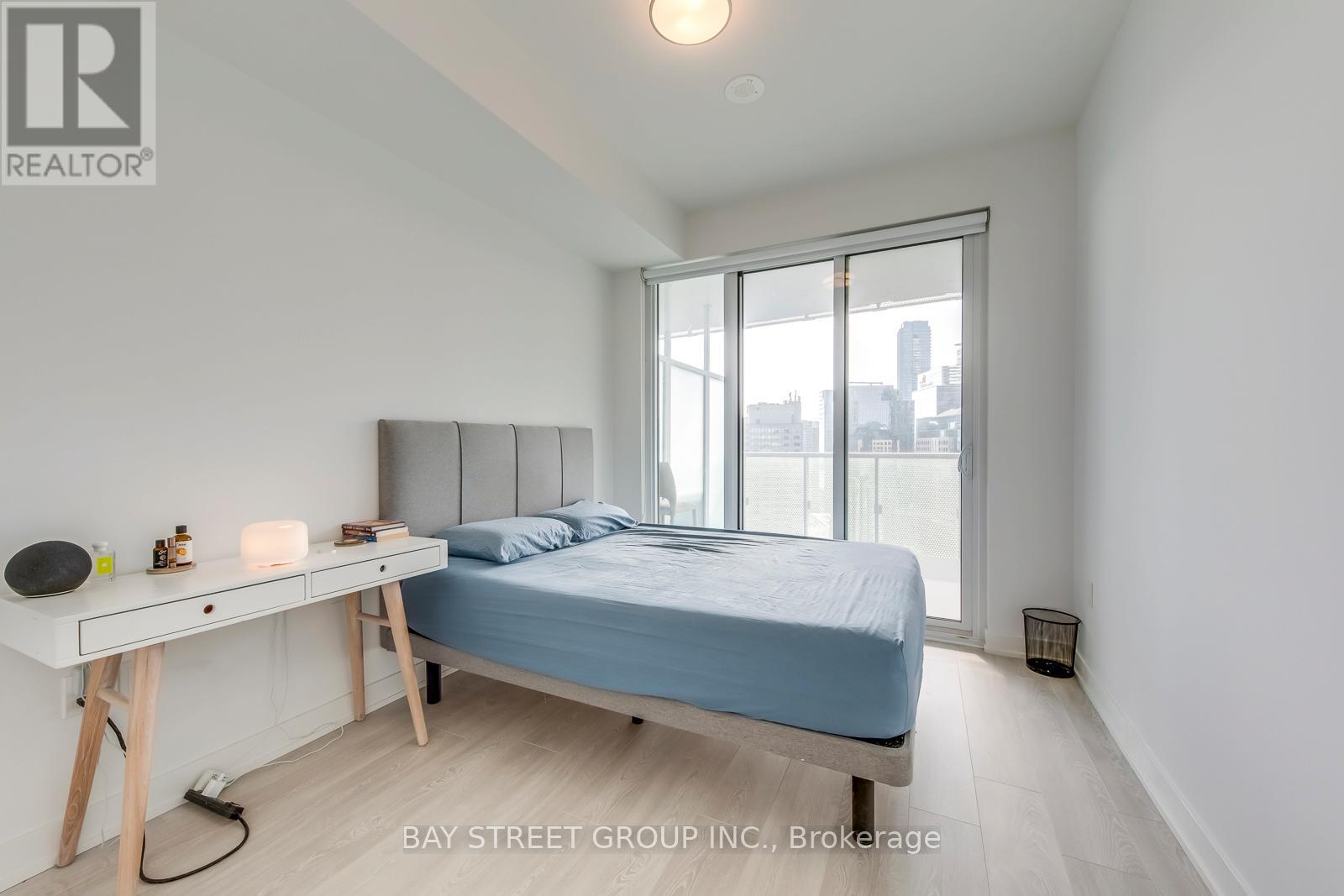 A bedroom with a bed, desk, and window overlooking a cityscape.