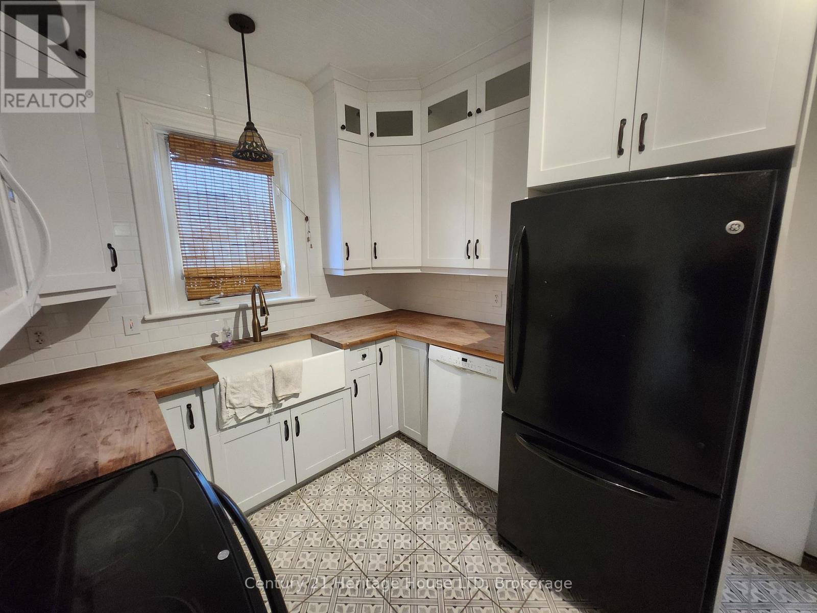 A black refrigerator is in a kitchen with white cabinets.