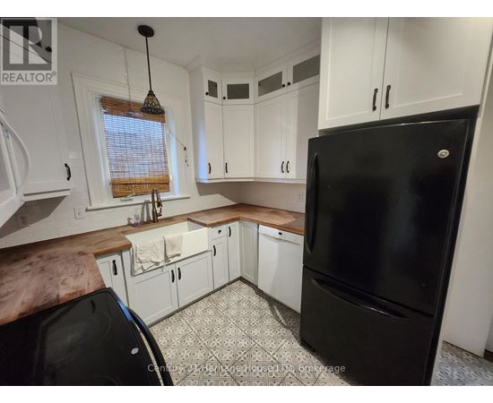 A black refrigerator is in a kitchen with white cabinets.