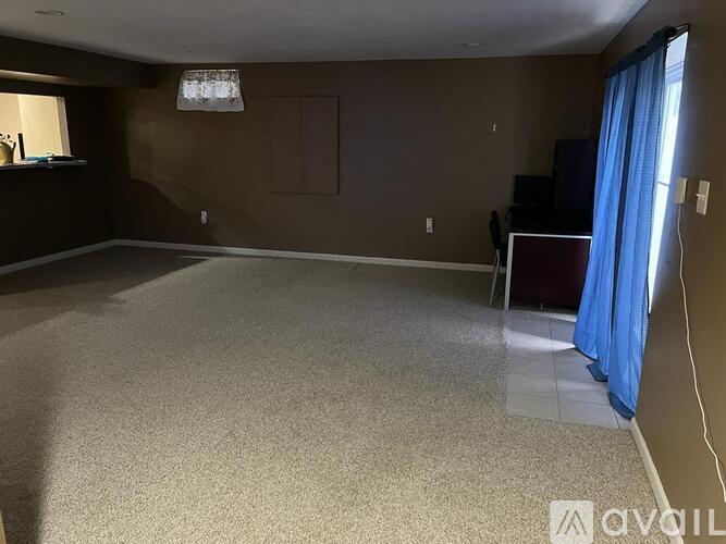 A living room with a carpeted floor and a window with blue curtains.