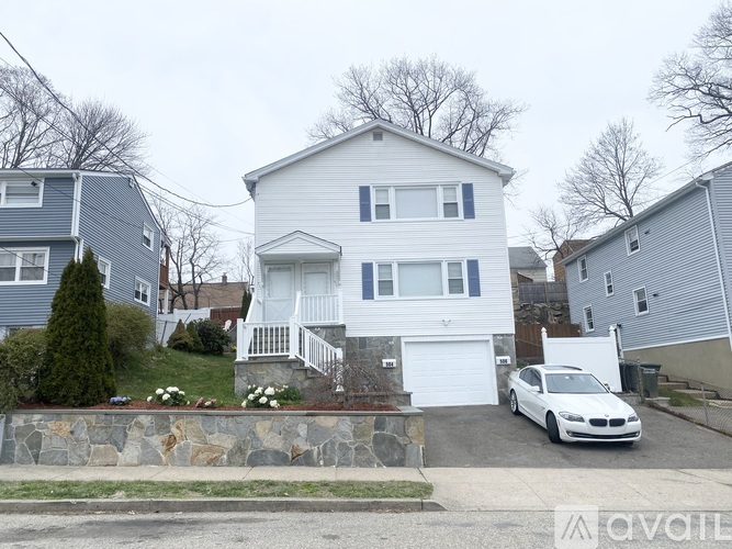 A white car is parked in front of a two-story house.