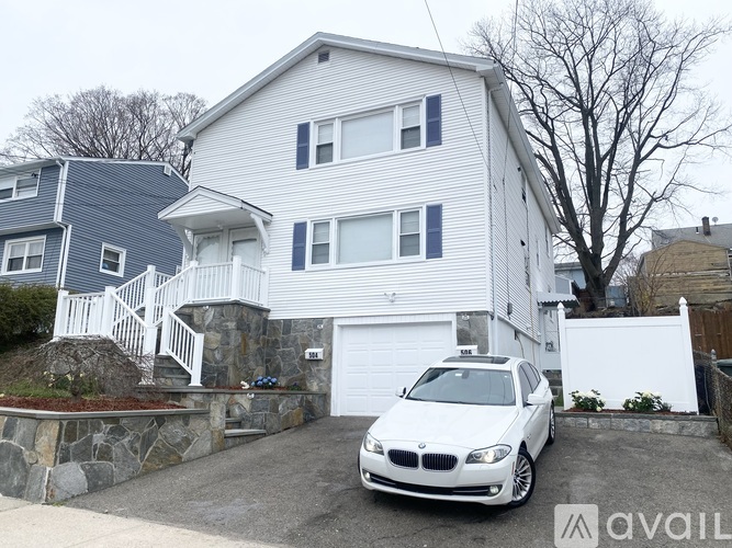 A white BMW car is parked in front of a two-story house.