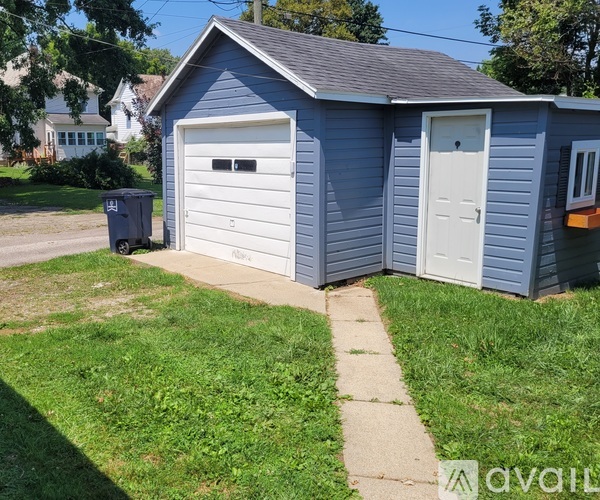A blue garage with a white door is situated on a grassy area.