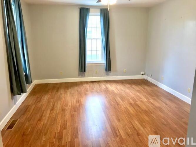 A room with wooden flooring and a window with green curtains.