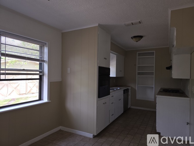 A kitchen with white cabinets and a window with blinds.