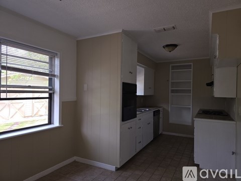 A kitchen with white cabinets and a window with blinds.
