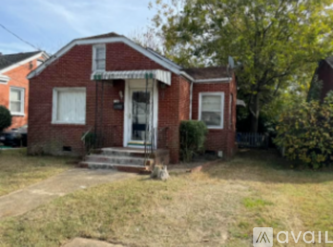 A red brick house with a front porch and a tree in front.