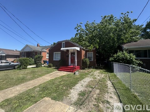 A red brick house with a front porch and a tree in front.