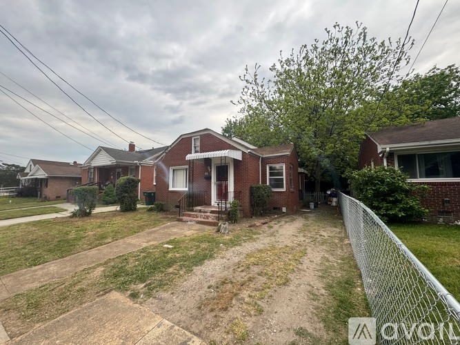 A house with a red brick exterior and a white door is surrounded by a chain link fence.