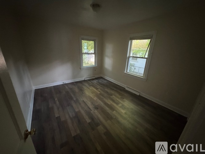 A room with wooden flooring and two windows.
